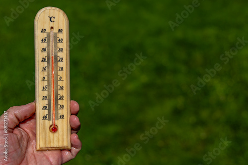 A man holds a wooden thermometer in his hand in the garden which indicates a very high temperature photo