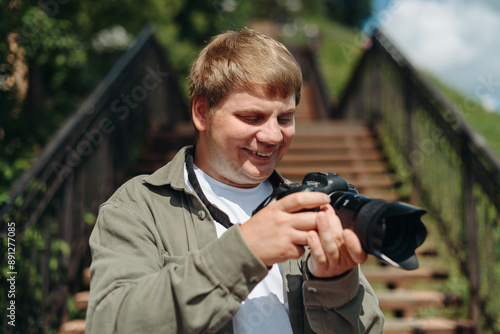 dslr camera in hands, young adult caucasian photographer in white t-shirt at work outdoors in sunny summer day