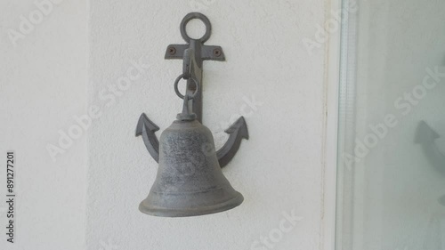 Medium shot: a man's hand striking an anchor-shaped bell, with diegetic audio.
