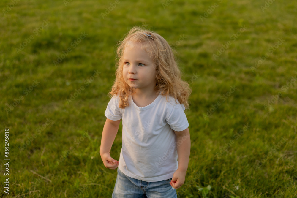 Cute blonde kid with curly hair walks on the lawn with soap bubbles in summer Cute blonde kid with curly hair walks on the lawn with soap bubbles in summer