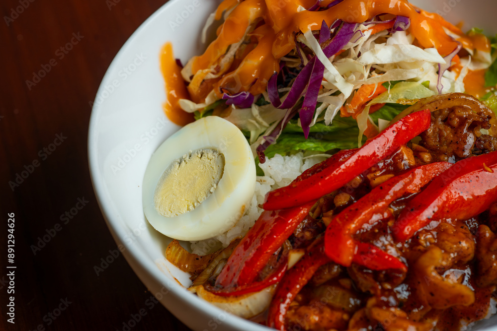 spicy blackpepper rice bowl, served with boiled egg, chili, and salad, on a white bowl, over wooden table spicy blackpepper rice bowl, served with boiled egg, chili, and salad, on a white bowl, over wooden table