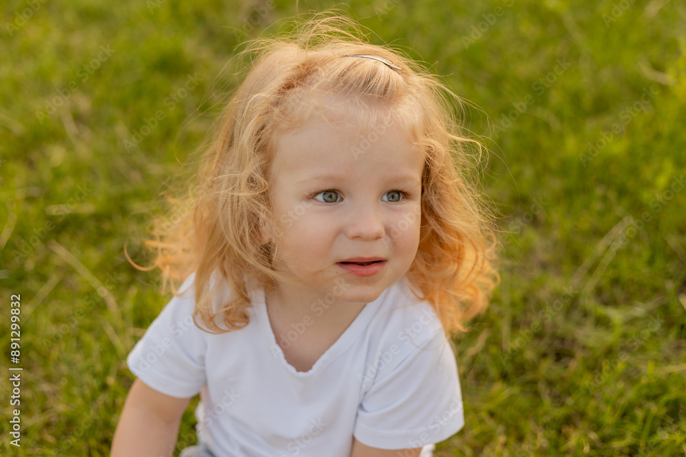 Cute blonde kid with curly hair walks on the lawn with soap bubbles in summer Cute blonde kid with curly hair walks on the lawn with soap bubbles in summer