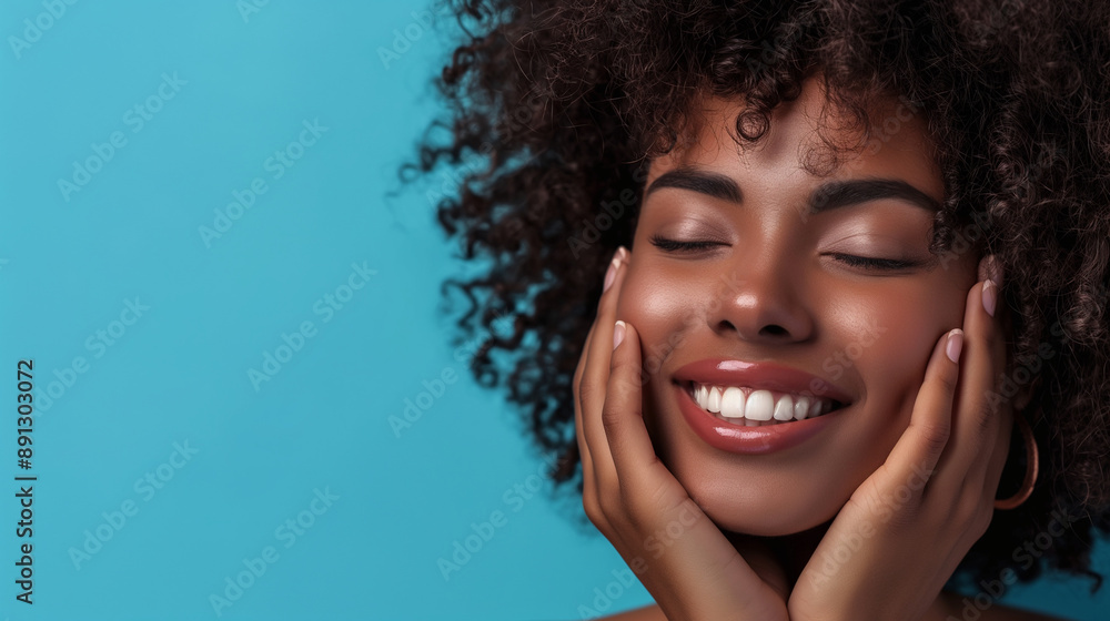 A smiling young black woman with natural curly hair beams brightly, her hands gently cradling her face, set against a striking blue background. A smiling young black woman with natural curly hair beams brightly, her hands gently cradling her face, set against a striking blue background.