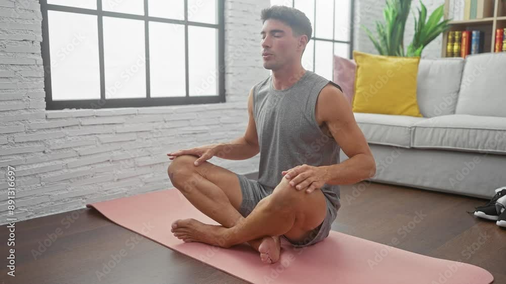 A serene young man meditating on a pink yoga mat in a well-lit living room, exuding tranquility and focus. A serene young man meditating on a pink yoga mat in a well-lit living room, exuding tranquility and focus.