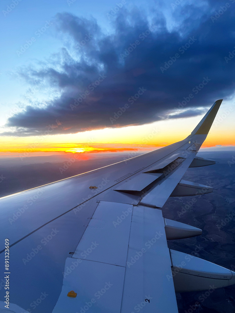 Fototapeta premium Orange Sunset View from an Airplane Window. A stunning view of the sunset from an airplane window, capturing the wing and the vibrant colors of the sky. 