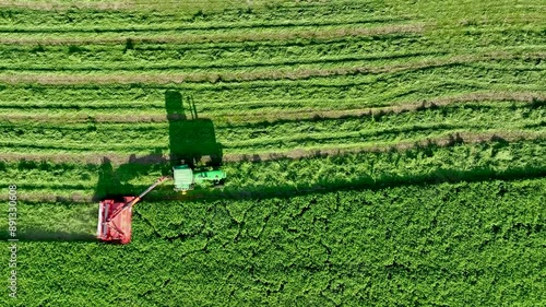 High-angle drone footage capturing a tractor harvesting hay crops in a lush green field. The video highlights the efficiency and precision of modern agricultural machinery in action