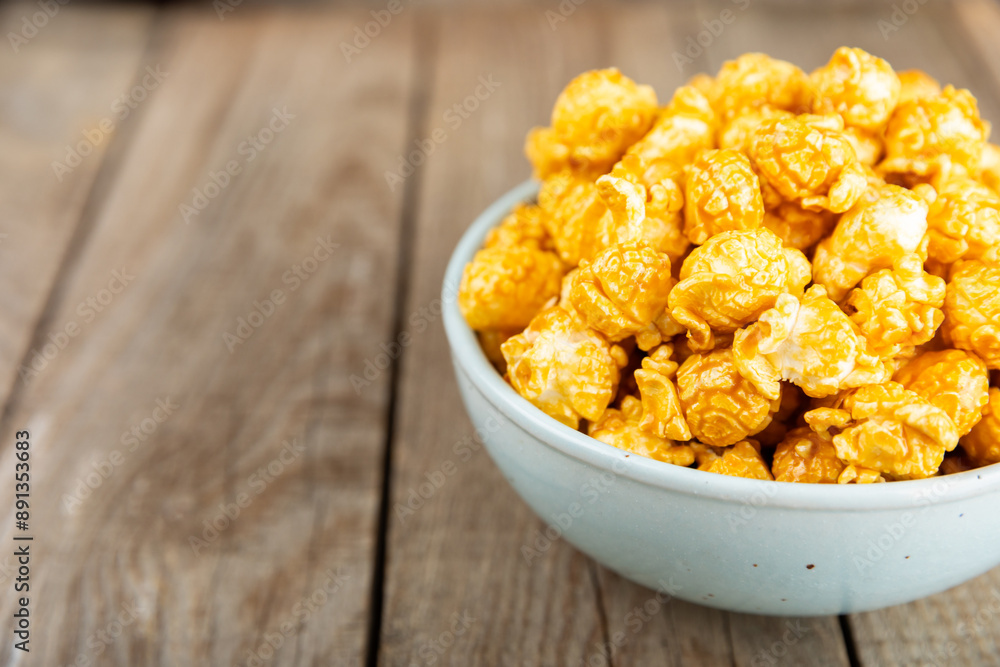 Sweet caramel popcorn in a bowl on a wooden background. Salted caramel popcorn. Caramel sauce. Close up. Topping. Place for text. Copy space Sweet caramel popcorn in a bowl on a wooden background. Salted caramel popcorn. Caramel sauce. Close up. Topping. Place for text. Copy space