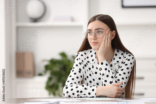 Embarrassed woman in glasses at table in office, space for text