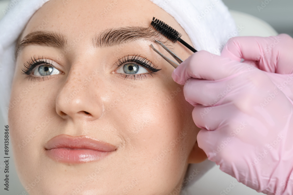 Beautician making eyebrow correction to young woman in beauty salon, closeup Beautician making eyebrow correction to young woman in beauty salon, closeup