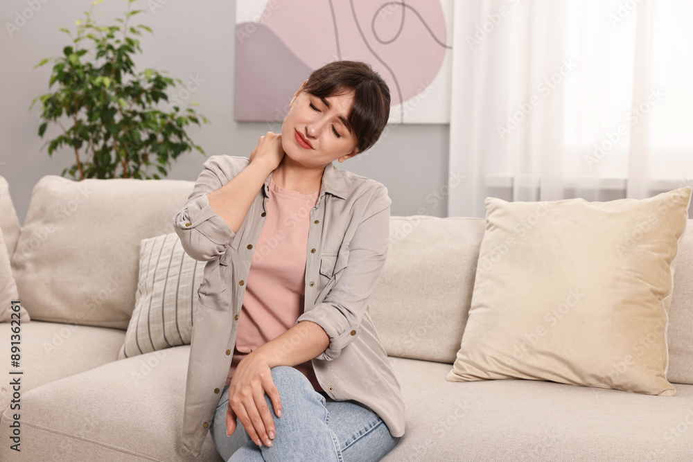 Upset woman suffering from neck pain on sofa at home Upset woman suffering from neck pain on sofa at home