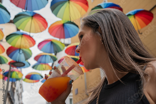 Young woman drinking juice under colorful umbrellas decoration. Young woman is enjoying a refreshing juice under a canopy of vibrant umbrellas