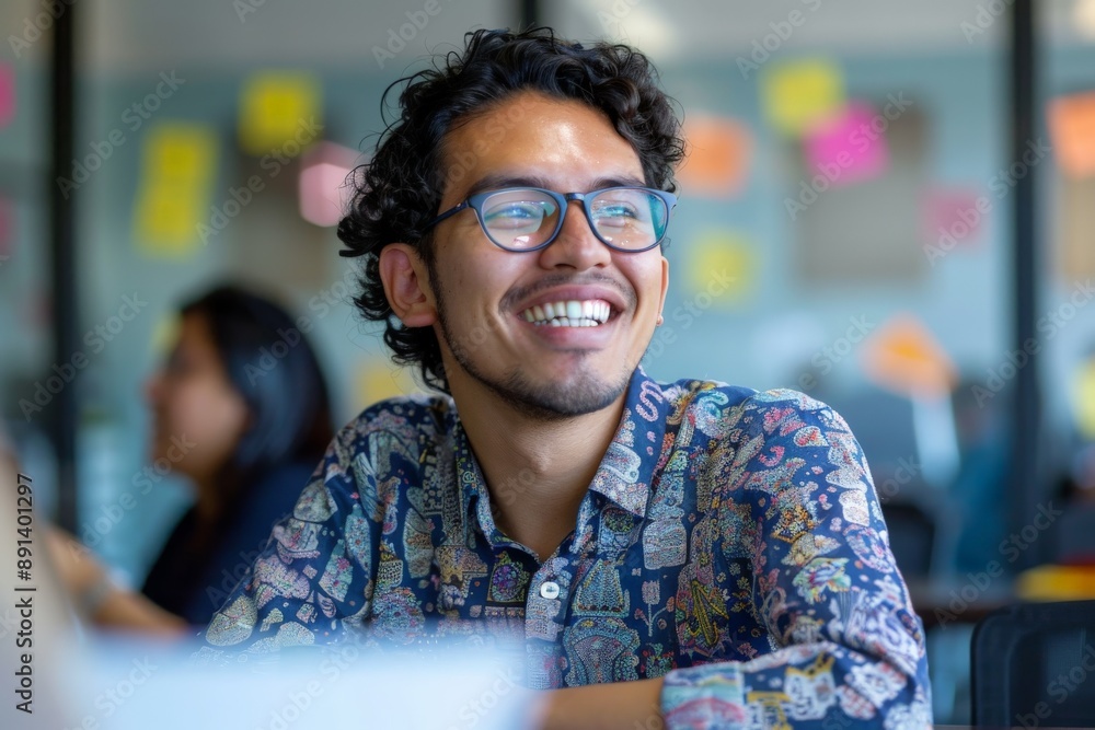 Fototapeta premium Hispanic male designer smiling looking up while working in busy open plan office