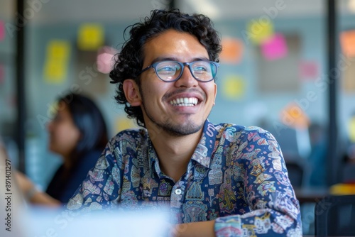 Hispanic male designer smiling looking up while working in busy open plan office photo