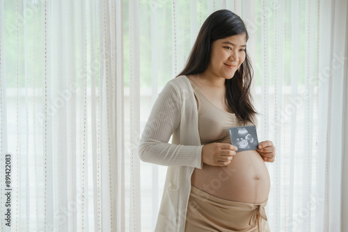 An Asian woman stands while pregnant with her first child, placing her hand on her stomach. She is excited and eagerly waiting for the birth day to meet her baby. Free Download An Asian woman stands while pregnant with her first child, placing her hand on her stomach. She is excited and eagerly waiting for the birth day to meet her baby. - GFXLoad