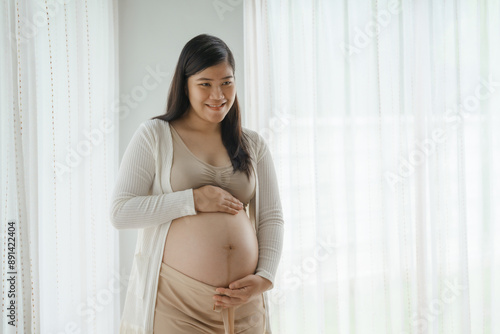 An Asian woman stands while pregnant with her first child, placing her hand on her stomach. She is excited and eagerly waiting for the birth day to meet her baby. Free Download An Asian woman stands while pregnant with her first child, placing her hand on her stomach. She is excited and eagerly waiting for the birth day to meet her baby. - GFXLoad