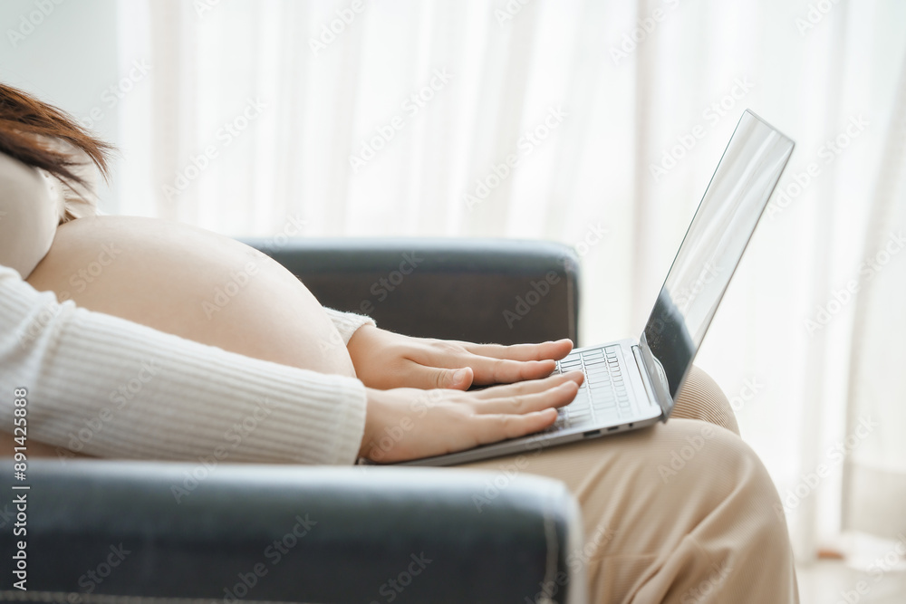 Naklejka premium A pregnant mother sits on the sofa, looking at her phone and shopping online. She is preparing to buy items for her unborn child, filled with anticipation and excitement for the arrival.