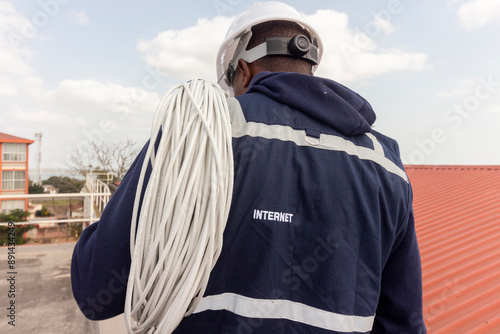 An African Technician on a Roof with Network Cables on His Shoulder, Connecting Internet at a Public Building
