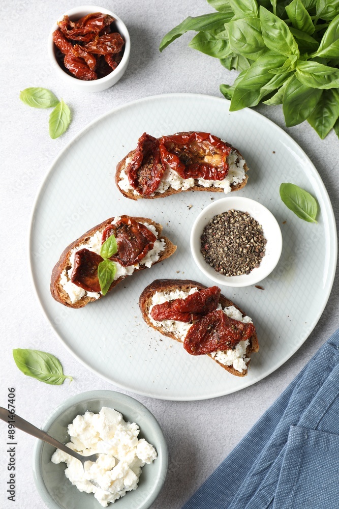 Delicious ricotta bruschettas with sun dried tomatoes, basil and milled pepper on light table, flat lay Delicious ricotta bruschettas with sun dried tomatoes, basil and milled pepper on light table, flat lay