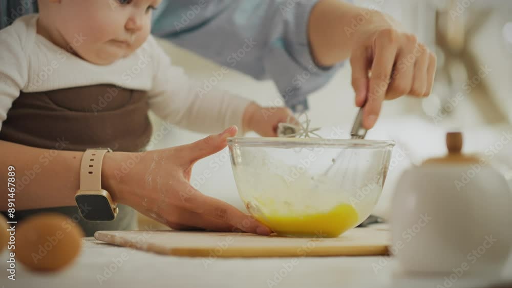Life style. Mom pastry chef using a whisk to beat eggs in the kitchen housing. Cinematic shot of Caucasian Asian girl preparing baking dough using modern sling for support, infant Life style. Mom pastry chef using a whisk to beat eggs in the kitchen housing. Cinematic shot of Caucasian Asian girl preparing baking dough using modern sling for support, infant