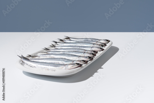 Photos Anchoas frescas dentro de un plato lleno de sal sobre mesa blanca y fondo azul