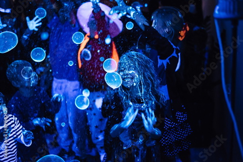 Children's disco. Children have fun at the soap bubble show. Fluorescent paint on the face in ultraviolet. Film noise. Diffuse focus. Halloween party