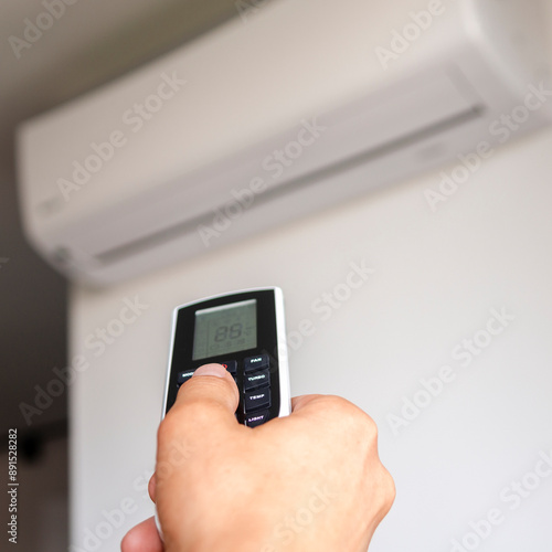 The remote control from the air conditioner is in the hand of a man against the background of the air conditioner. Climate control