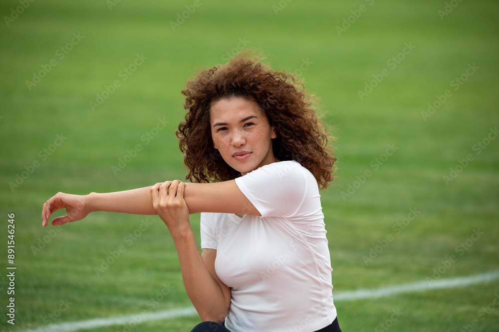 Curly beautiful Asian girl in a white T-shirt and black leggings plays sports on the football field Curly beautiful Asian girl in a white T-shirt and black leggings plays sports on the football field