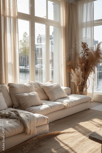 Spacious living room with bright and airy feel, large windows showcasing a waterfront view, light-colored decor, and soft throws, offering a serene and inviting ambiance. photo