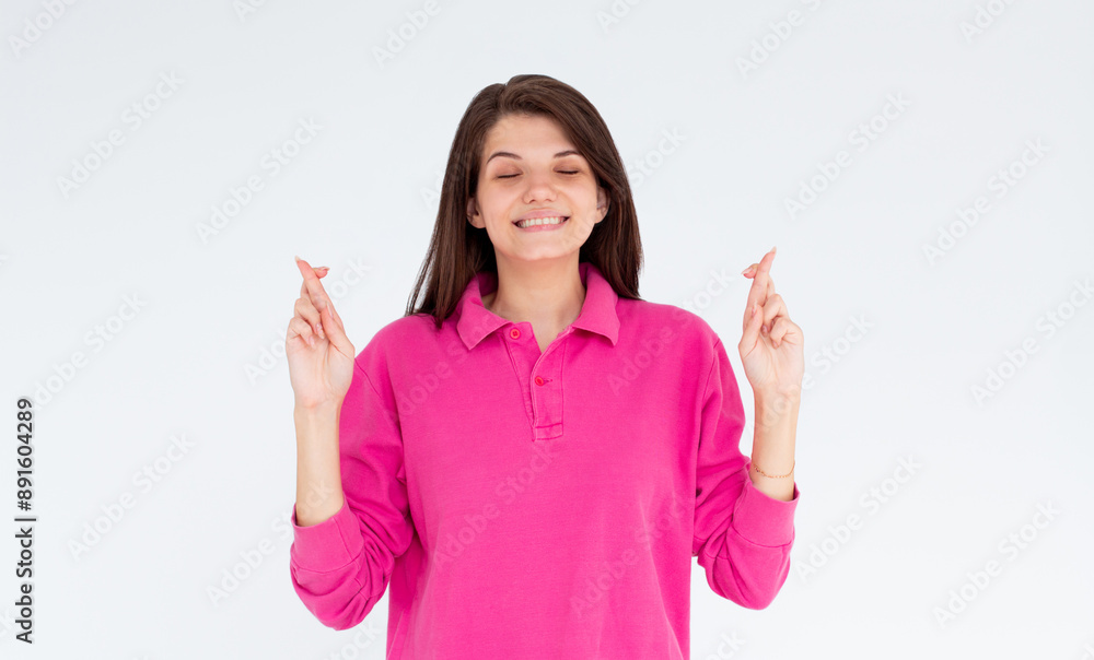 Intrigued woman in pink long sleeve praying with crossed fingers and closed eyes over white background Intrigued woman in pink long sleeve praying with crossed fingers and closed eyes over white background