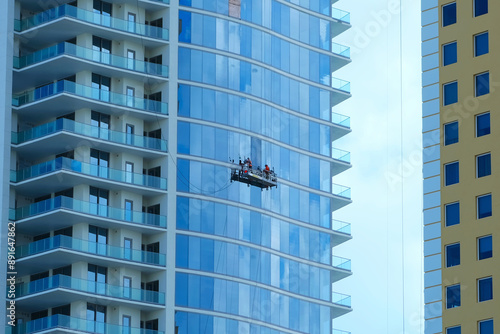 Canvas Print Workers on an outside suspended scaffold platform cleaning a skyscraper building facade with glass windows and balconies