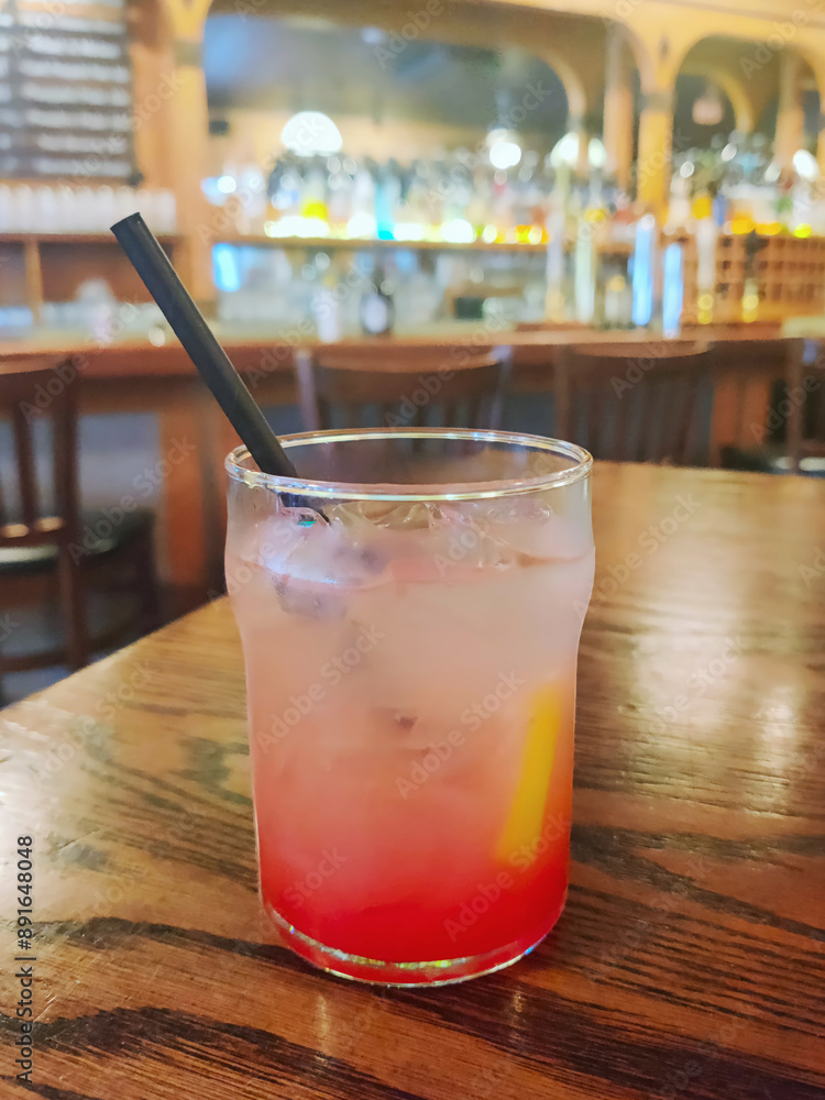 Glass of lemonade with ice and straw on wooden bar table in dimly lit pub. Glass of lemonade with ice and straw on wooden bar table in dimly lit pub.
