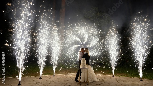 Completion of the wedding, newlyweds cutting the cake, fireworks. Newlyweds cutting a cake against the backdrop of cold lights in the evening. Cold lights, newlyweds, cake.