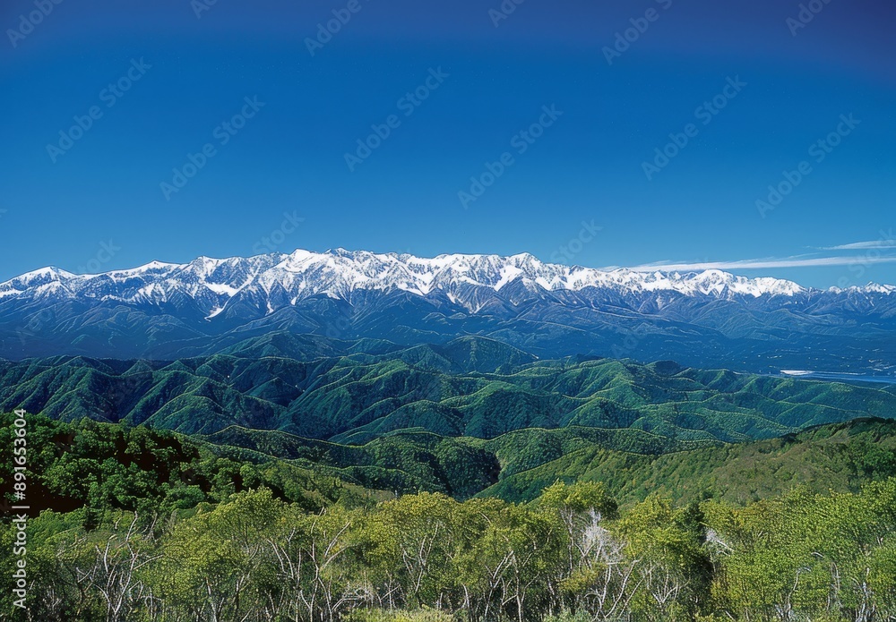 Fototapeta premium mountain range from an angle, clear blue sky, distant snow-capped mountains in background