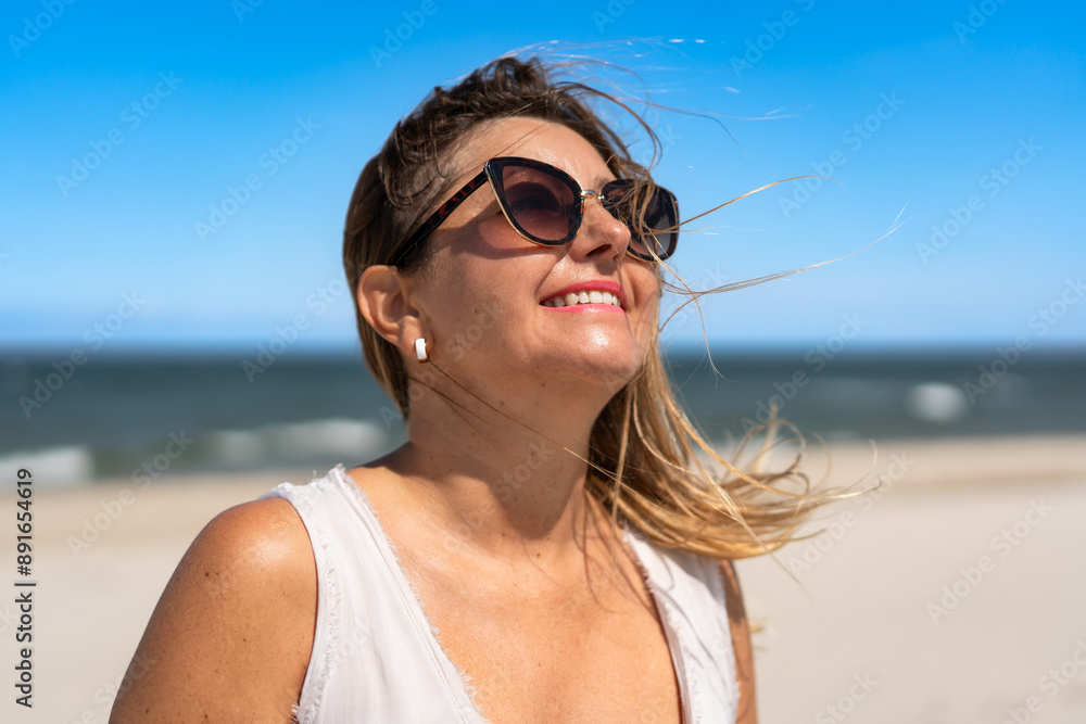 Summer. Portrait of young beautiful smiling woman with long blonde hair in light top and sunglasses facing sun against background of beach and sea. Energy, joy of life and youth. Summer. Portrait of young beautiful smiling woman with long blonde hair in light top and sunglasses facing sun against background of beach and sea. Energy, joy of life and youth.