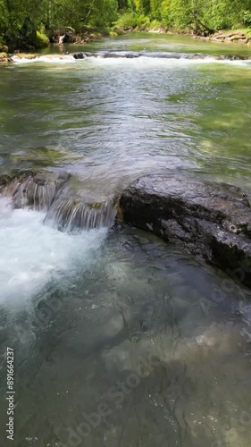 Aerial Drohnenflug rückwärts in niedriger Höhe über eine Stromschnelle in einem Fluss mit kristallklarem Wasser in den Alpen, Hochformat, UHD photo