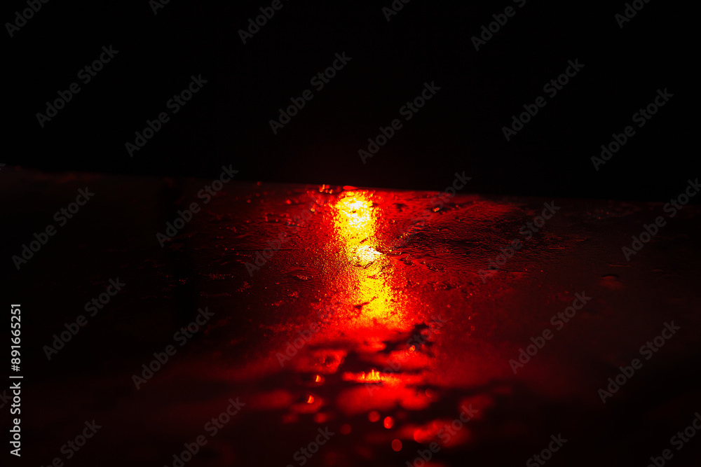 Red light is reflected in the water during the night. The scene is dark and moody. Red light shining through rain on dark surface, creating a moody and atmospheric scene