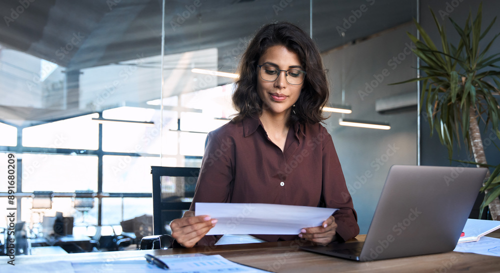© Stock 4 You - Focused latin hispanic young business woman working on laptop computer reading financial document report in office. Accountant entrepreneur manager businesswoman doing paperwork using pc. Copy space