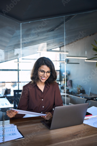 Free Download 30s accountant entrepreneur manager businesswoman doing paperwork using pc. Smiling latin hispanic young business woman working on laptop computer reading financial document report in office. Vertical - GFXLoad