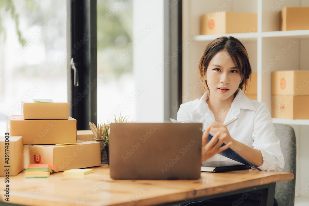 Young beautiful happy asian business woman owner of SME online using laptop receive order from customer with parcel box packaging at her startup Young beautiful happy asian business woman owner of SME online using laptop receive order from customer with parcel box packaging at her startup