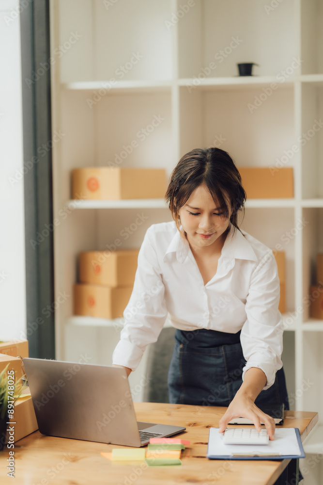 Young beautiful happy asian business woman owner of SME online using laptop receive order from customer with parcel box packaging at her startup Young beautiful happy asian business woman owner of SME online using laptop receive order from customer with parcel box packaging at her startup