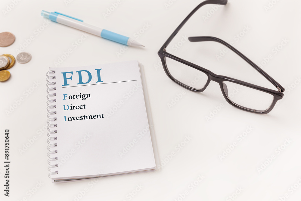The Foreign Direct Investment concept with letters FDI written on notebook and business office items like pen, coins, and glasses The Foreign Direct Investment concept with letters FDI written on notebook and business office items like pen, coins, and glasses