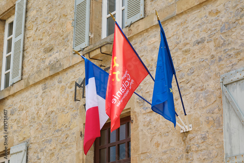 Three flags on the natural stone wall of the town hall or la mairie of the village of Cornac Lot Occitanie in Southern France. The flag of France, Occitanie and Europe photo