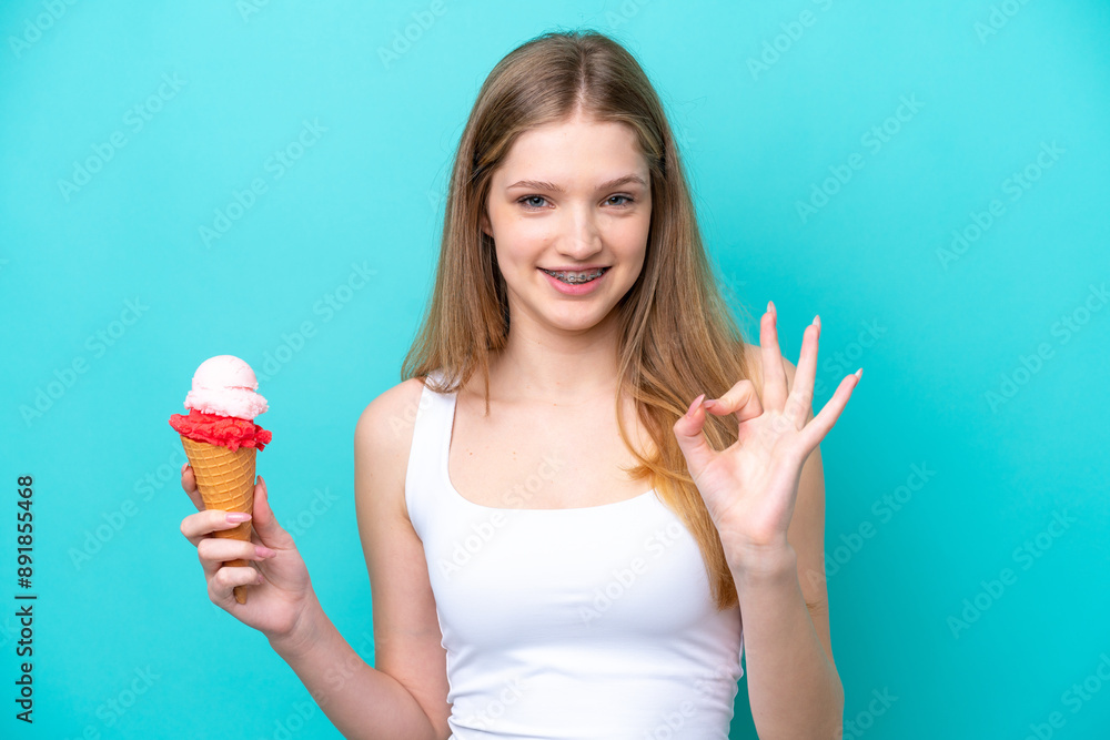 Teenager Russian girl with a cornet ice cream isolated on blue background showing ok sign with fingers Teenager Russian girl with a cornet ice cream isolated on blue background showing ok sign with fingers