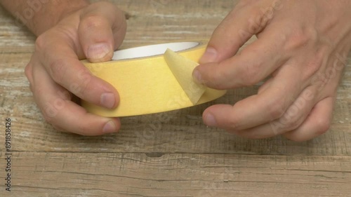 Hands tightly grip yellow masking tape on a table with various DIY tools in a crafting workspace