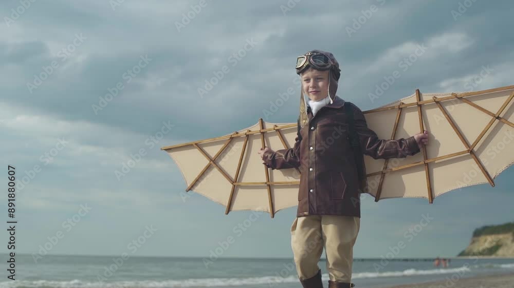 Little boy in pilot suit with artificial wings on his back walks along seashore. Little boy in pilot suit with artificial wings on his back walks along seashore.