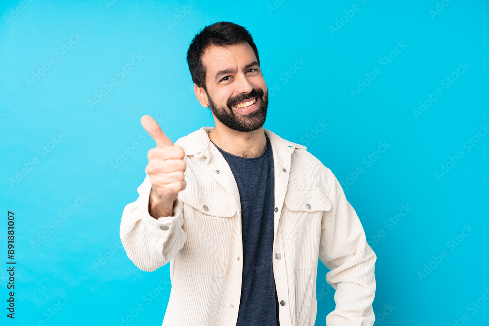Young handsome man with white corduroy jacket over isolated blue background with thumbs up because something good has happened Young handsome man with white corduroy jacket over isolated blue background with thumbs up because something good has happened
