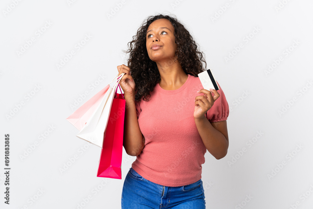 Teenager cuban girl isolated on white background holding shopping bags and a credit card and thinking Teenager cuban girl isolated on white background holding shopping bags and a credit card and thinking