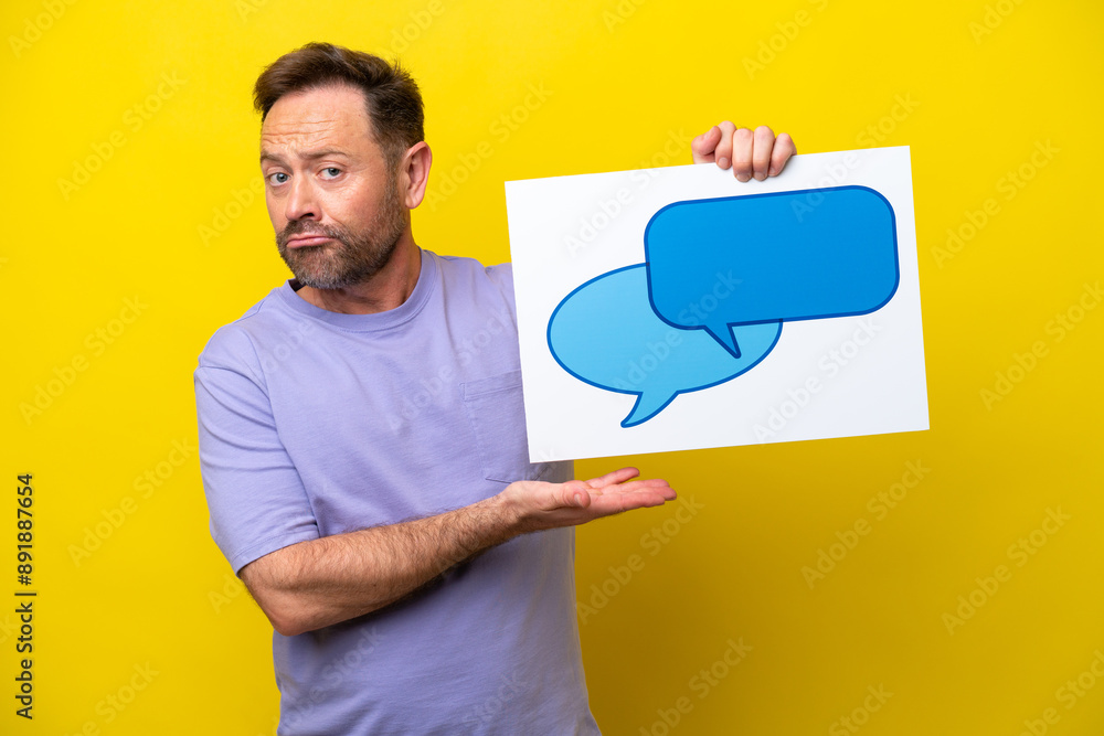 Middle age caucasian man isolated on yellow background holding a placard with speech bubble icon and pointing it Middle age caucasian man isolated on yellow background holding a placard with speech bubble icon and pointing it
