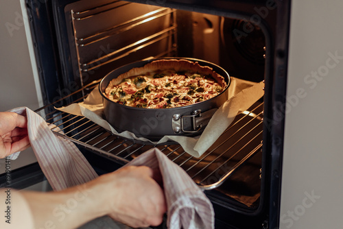 Konstfotografi A man uses a kitchen towel to take out of the oven a baked quiche lorraine, a tr