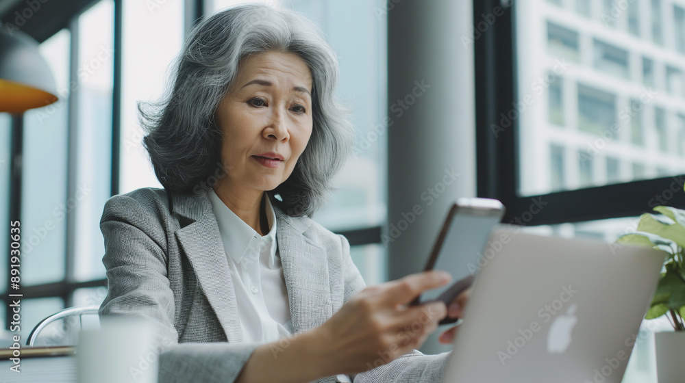 Senior middle aged Asia businesswoman manager ceo using smartphone and laptop in office working online Senior middle aged Asia businesswoman manager ceo using smartphone and laptop in office working online